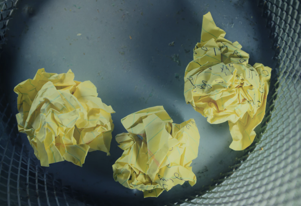 Picture of three crumbled up balls of yellow paper in a rubbish bin